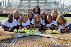 a group of women pose for a photo on the field with softball bats and balls