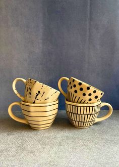 three ceramic cups with black and white designs on them sitting in front of a blue wall