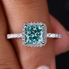 a woman's hand holding a ring with a blue and white diamond in it