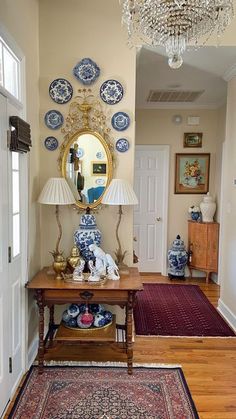 an entryway with blue and white plates on the wall, a table with a lamp, and a chandelier