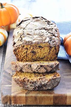 sliced pumpkin bread sitting on top of a wooden cutting board next to some pumpkins