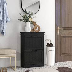 a black cabinet sitting in front of a mirror next to a white vase with flowers