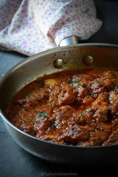 a pan filled with meat and sauce on top of a wooden table next to a napkin