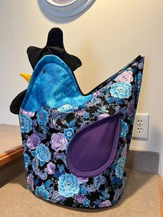 a blue bird sitting on top of a black and purple flowered bag next to a clock