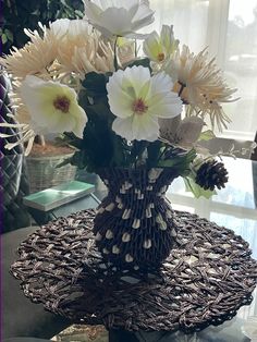 a vase filled with lots of white flowers on top of a table next to a window