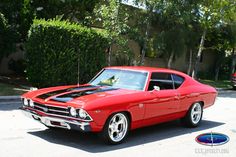 a red muscle car parked in front of a house