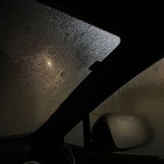 the inside of a car that is covered in rain and light shining down on it