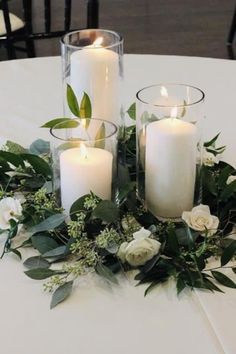 three candles are sitting on a table with flowers and greenery