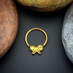 a gold ring with a bow on it sits next to some rocks and stones in the background