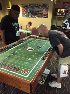 two men playing a game of football on a table in a sports room with other people