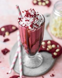 a red drink with whipped cream and sprinkles in it next to cookies