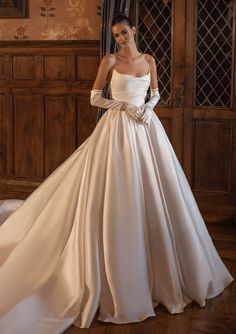 a woman in a white wedding dress standing next to a wooden paneled wall and wearing gloves