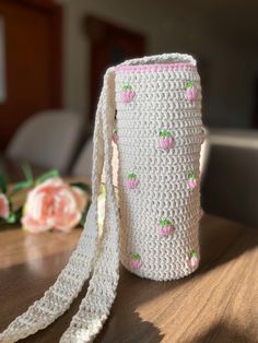 a crocheted roll with pink flowers on it sitting on a table next to a flower vase