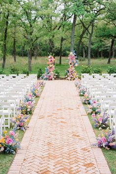 an outdoor ceremony with rows of white chairs and colorful flowers on the aisle, surrounded by trees