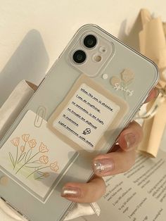 a woman is holding up her phone case with flowers on it and an open book in the background