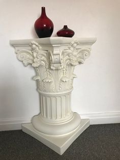 a white pedestal with two red vases sitting on it's top and bottom