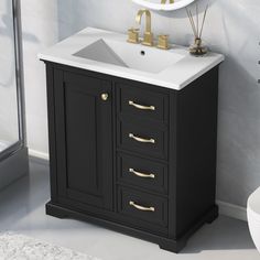 a white sink sitting under a mirror next to a black cabinet with gold handles and drawers