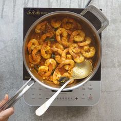 a person holding a spoon over a pot filled with shrimp