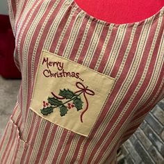 a red and white striped christmas apron with holly decorations on the front, saying merry christmas