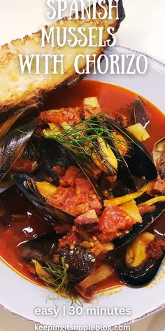 spanish mussels with chorizo in a white bowl next to bread on a table