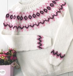 a white sweater with pink and black designs on it sitting next to a flower pot