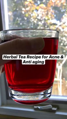 a hand holding a glass filled with red liquid and the words herb tea recipe for acne & anti aging