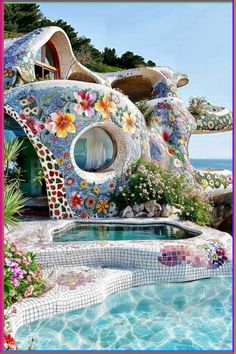 an artisticly designed house by the ocean with flowers on it's roof and windows