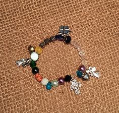 a close up of a bracelet with beads and charms on a fabric background, showing the cross