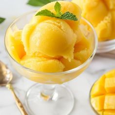 mango ice cream in a glass bowl with mint garnish on the rim and spoons next to it