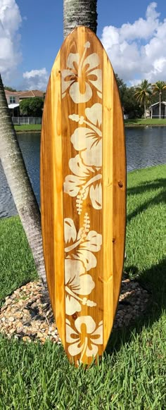 a wooden surfboard sitting in the grass next to a palm tree and body of water