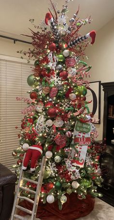 a christmas tree is decorated with red, green and silver ornaments while a ladder stands in front of it