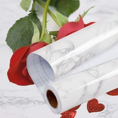 two rolls of white marble paper next to a red rose with hearts on the floor