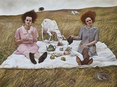 two women sitting on a blanket in the middle of a field eating food and drinking tea