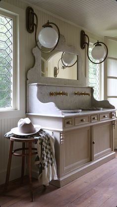 a white sink sitting under a bathroom mirror next to a wooden table with a hat on it