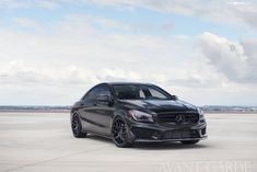 a black mercedes cla parked on top of an airport tarmac with clouds in the background