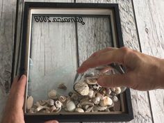 a person holding a glass jar filled with seashells on top of a wooden table