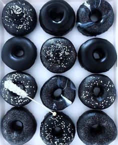 a box filled with black donuts covered in sprinkles and white frosting