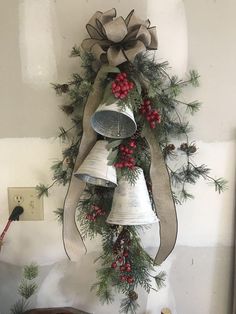 a bunch of bells hanging from the side of a wall with pine cones and berries