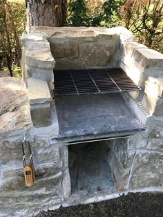 an outdoor bbq grill built into the side of a stone wall in front of a tree