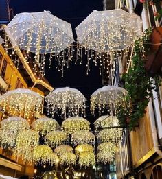 several white umbrellas hanging from the ceiling in front of a building with lights on it