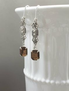 Textured Front, Hollow Back These elegant flapper earrings feature Deco style brass connectors and beautiful smoky topaz (warm brown) glass beads. The antiqued silver brass connectors have a textured front and a hollow reverse side. (SEE 2nd PHOTO) The earrings are extremely lightweight and comfortable to wear; perfect for your next 1920s themed event or everyday. These dainty dangles are 2 inches long and hang from silver plated lever back ear wires. ABOUT THIS COLLECTION What are the three sty Flapper Aesthetic, Art Deco Jewelry 1920s, 1920s Earrings, Gold Art Deco Earrings, Teardrop Pearl Earrings, Downton Abbey Fashion, Peach Art, Smoky Topaz, Historical Jewellery