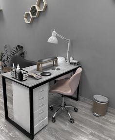 a desk with a chair, lamp and other items on it in front of a gray wall