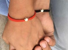 two people holding hands with red string and white arrow bracelets on their wristes