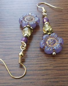 two pairs of purple and gold beaded earrings on a wooden table with metal hooks