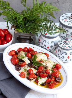 a white plate topped with lots of food next to two bowls filled with tomatoes and olives