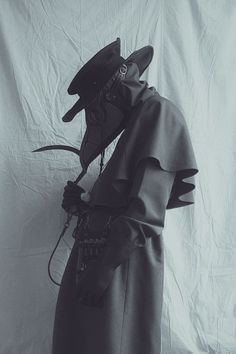 a black and white photo of a man in a trench coat with a hat on his head