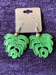 green crocheted earrings with wooden beads on purple fabric next to cardboard card and tag