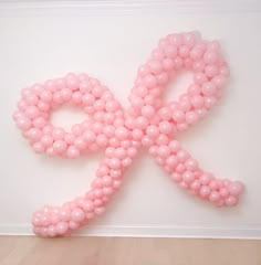 a pink ribbon made out of balloons sitting on top of a wooden floor next to a white wall