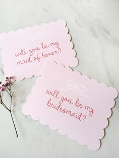 two bridesmaid cards on a marble table with pink flowers in the foreground