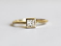 a yellow gold engagement ring with a princess cut diamond set in the center, on a white background